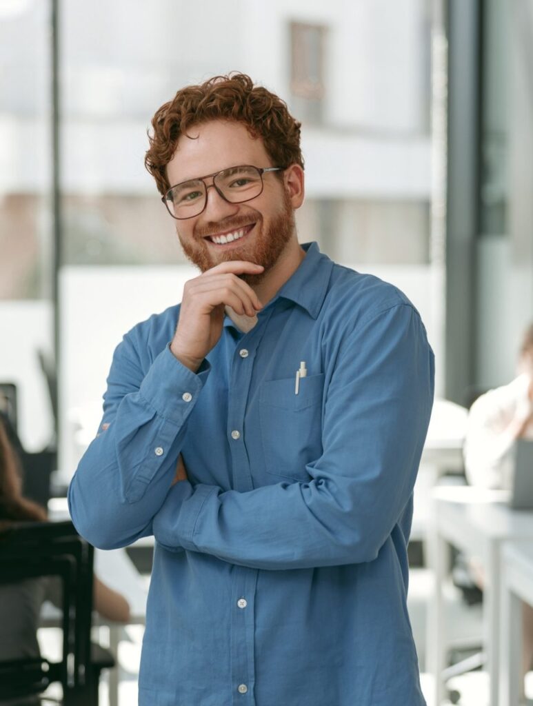 Handsome businessman in eyeglasses looking on camera with smile standing on office background