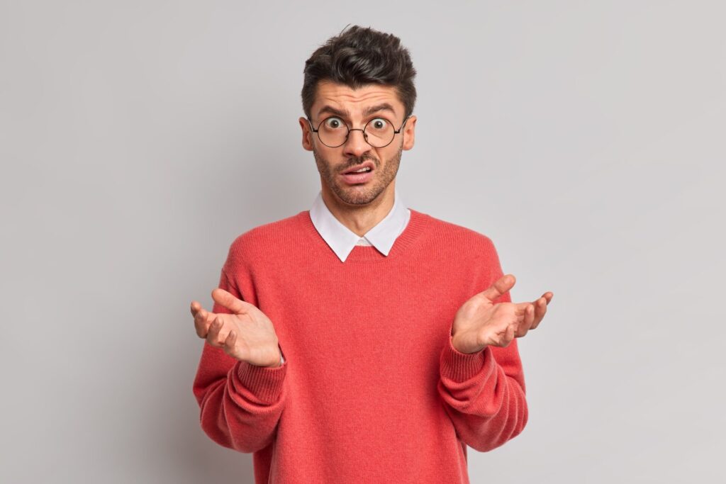 Indignant puzzled man raises palms and faces difficult choice feels hesitant wears round transparent