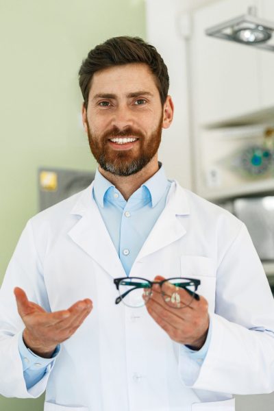 Portrait of ophthalmologist offering glasses to client in optics store